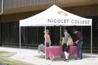 Two students look at materials on a table under a tent with Nicolet College printed on it