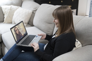 A student sitting on a white couch speaks with a success coach on her laptop.