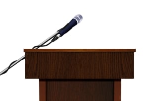 A wooden speaker podium and microphone, against a white background, with no speaker behind it. 